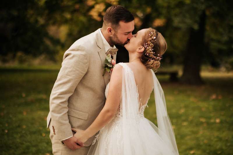 Hochzeitsfotograf-Rudolstadt (67)-Heiraten Das Brautpaar hält sich bei den Händen und küsst sich zart auf einer grünen Wiese mit erstem Herbstlaub